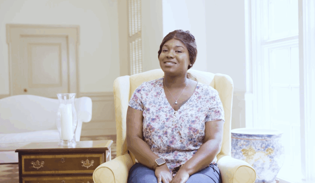 Woman sitting in bright room, smiling.